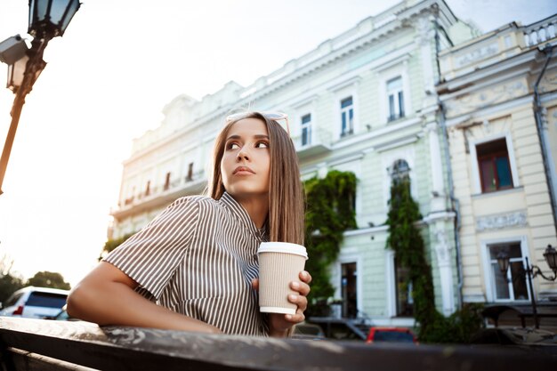 Joven hermosa mujer sentada en el banco, sosteniendo el café.