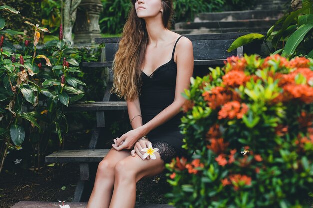 Joven hermosa mujer sexy en jardín tropical, vacaciones de verano en Tailandia, delgado cuerpo bronceado flaco, vestidito negro con encaje, aspecto natural, sensual, relajado,