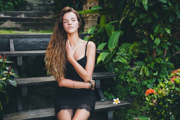 Joven hermosa mujer sexy en jardín tropical, vacaciones de verano en Tailandia, delgado cuerpo bronceado flaco, vestidito negro con encaje, aspecto natural, sensual, relajado,
