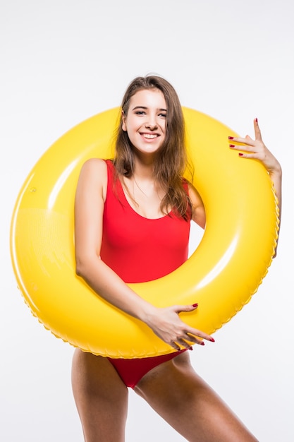 Joven hermosa mujer sexy en traje de baño rojo tiene colchón de aire amarillo redondo aislado sobre fondo blanco