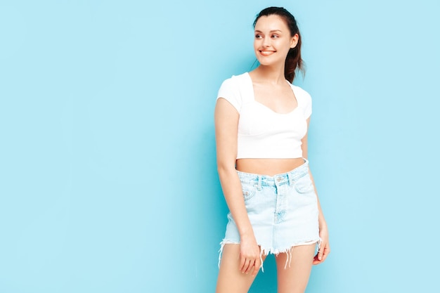 Joven hermosa mujer sonriente en falda de jeans de verano de moda y ropa superior Mujer despreocupada sexy posando junto a la pared azul en el estudio Modelo morena positiva divirtiéndoseAlegre y feliz