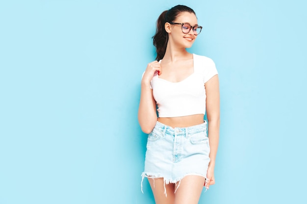 Joven hermosa mujer sonriente en falda de jeans de verano de moda y ropa superior Mujer despreocupada sexy posando junto a la pared azul en el estudio Modelo morena positiva divirtiéndoseAlegre y feliz