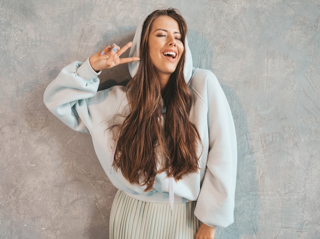 Joven hermosa mujer sonriente mirando. Chica de moda en ropa casual de verano con capucha y falda. . Mostrando signo de paz