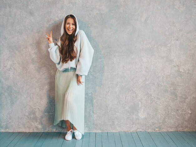 Joven hermosa mujer sonriente mirando. Chica de moda en ropa casual de verano con capucha y falda. . Mostrando signo de paz