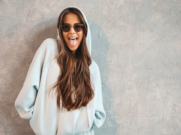 Joven hermosa mujer sonriente mirando. Chica de moda en ropa casual de verano con capucha y falda. Muestra lengua