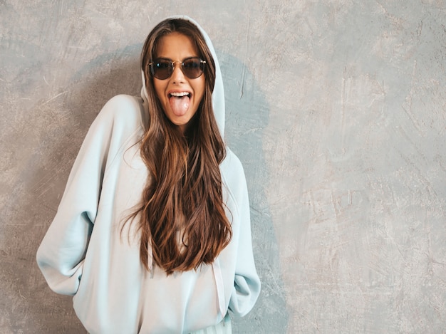 Joven hermosa mujer sonriente mirando. Chica de moda en ropa casual de verano con capucha y falda. Muestra lengua