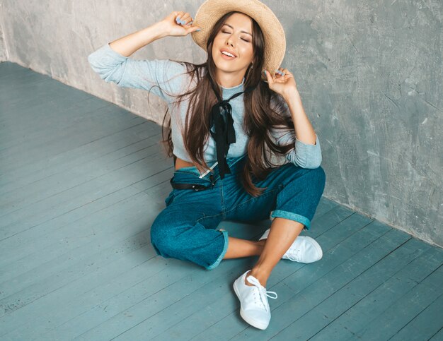 Joven hermosa mujer sonriente mirando. Chica de moda en ropa casual de verano y sombrero. Sentado en el suelo