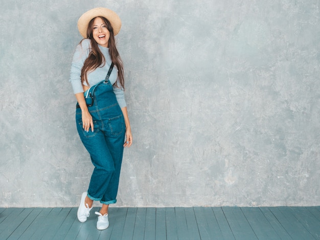 Joven hermosa mujer sonriente mirando. Chica de moda en ropa de verano casual monos y sombrero.