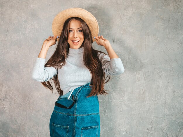 Joven hermosa mujer sonriente mirando. Chica de moda en ropa de verano casual monos y sombrero.