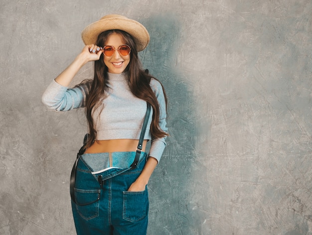 Joven hermosa mujer sonriente mirando. Chica de moda en ropa de verano casual monos y sombrero.