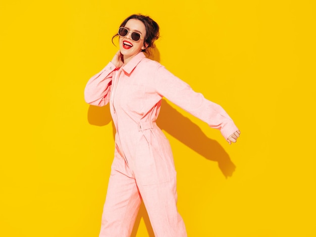 Joven hermosa mujer sonriente en mono rosa de verano de moda Mujer sexy despreocupada posando cerca de la pared amarilla en el estudio Modelo positivo divirtiéndose y volviéndose loco Alegre y feliz Bailando