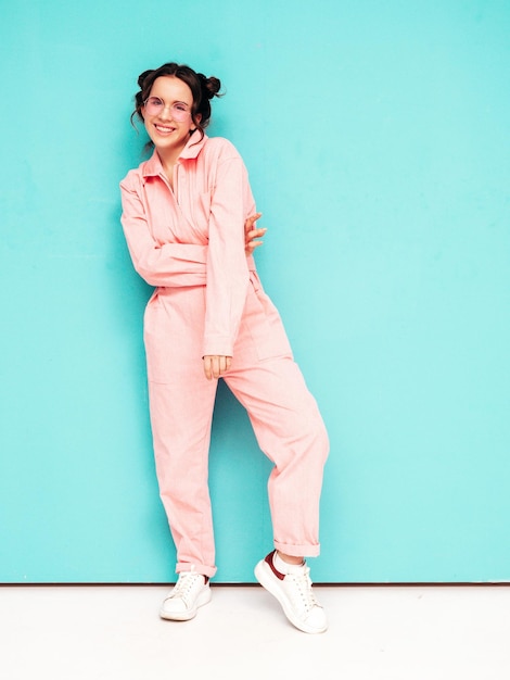 Joven hermosa mujer sonriente en un mono rosa de verano de moda Sexy mujer despreocupada posando junto a la pared azul en el estudio con dos cuernos Modelo positivo divirtiéndose y volviéndose loco Alegre y feliz