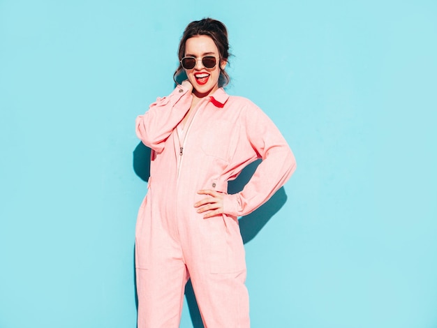 Joven hermosa mujer sonriente en un mono rosa de verano de moda Sexy mujer despreocupada posando junto a la pared azul en el estudio con dos cuernos Modelo positivo divirtiéndose y volviéndose loco Alegre y feliz