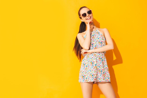 Foto gratuita joven hermosa mujer sonriente en monos de verano de moda mujer sexy con posando cerca de la pared amarilla en el estudio modelo positivo divirtiéndose alegre y feliz