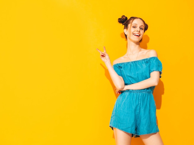 Joven hermosa mujer sonriente en overoles de jeans de verano de moda Mujer sexy despreocupada con peinado de dos cuernos posando junto a la pared amarilla en el estudio Modelo positivo divirtiéndose Aislado