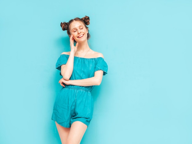 Joven hermosa mujer sonriente en overoles de jeans de verano de moda Mujer sexy despreocupada con peinado de dos cuernos posando junto a la pared en el estudio Modelo positivo divirtiéndose Alegre y feliz Aislado