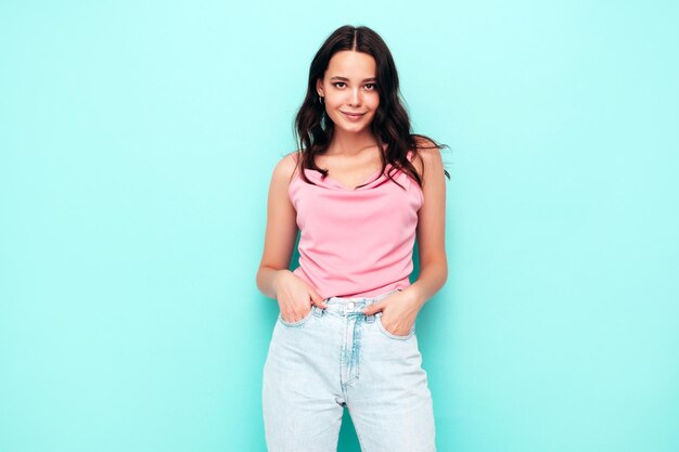 Joven hermosa mujer sonriente en ropa de verano de moda Mujer sexy despreocupada posando junto a la pared azul en el estudio Modelo morena positiva divirtiéndose y volviéndose loca Alegre y feliz