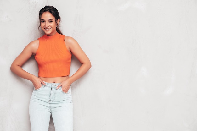 Joven hermosa mujer sonriente en ropa de verano de moda Mujer sexy despreocupada posando junto a la pared gris en el estudio Modelo morena positiva divirtiéndose y volviéndose loca Alegre y feliz