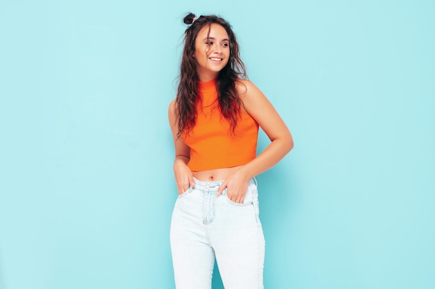 Joven hermosa mujer sonriente en top naranja de verano de moda y ropa de jeansSexy mujer despreocupada posando junto a la pared azul en el estudio Modelo morena positiva divirtiéndose y volviéndose loca Alegre y feliz