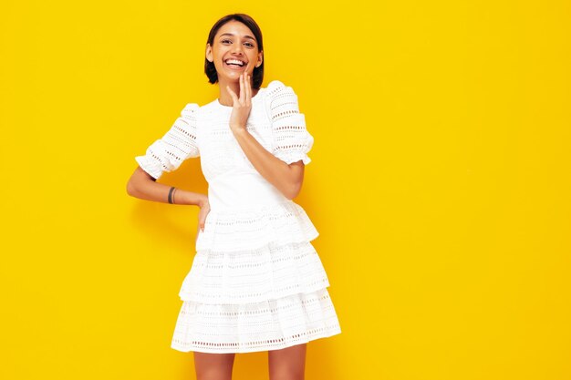 Joven hermosa mujer sonriente en vestido blanco de verano de moda Sexy mujer despreocupada posando junto a la pared amarilla en el estudio Modelo positivo divirtiéndose Alegre y feliz Aislado