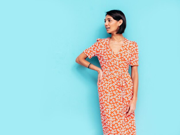 Joven hermosa mujer sonriente en vestido rojo de verano de moda Mujer despreocupada sexy posando junto a la pared azul en el estudio Modelo positivo divirtiéndose Alegre y feliz Aislado