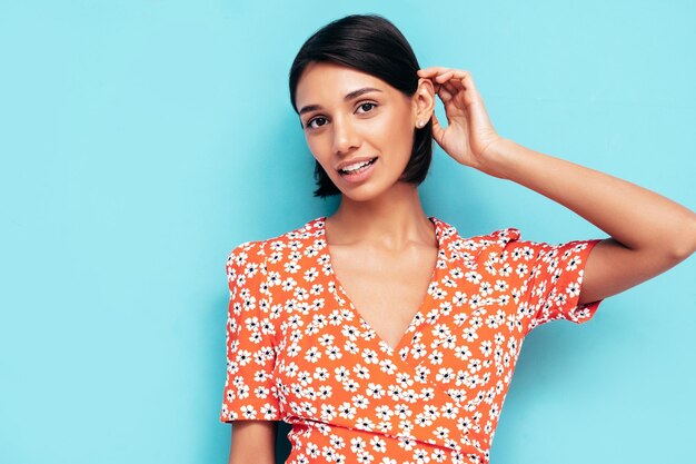 Joven hermosa mujer sonriente en vestido rojo de verano de moda Mujer despreocupada sexy posando junto a la pared azul en el estudio Modelo positivo divirtiéndose Alegre y feliz Aislado