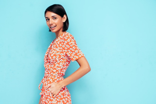 Foto gratuita joven hermosa mujer sonriente en vestido rojo de verano de moda mujer despreocupada sexy posando junto a la pared azul en el estudio modelo positivo divirtiéndose alegre y feliz aislado