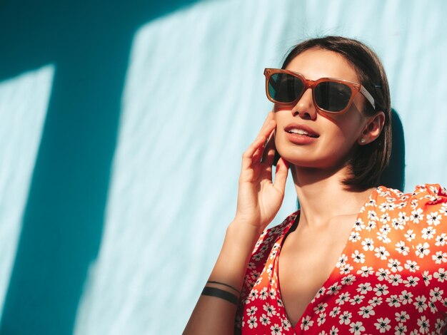 Joven hermosa mujer sonriente en vestido rojo de verano de moda Sexy mujer despreocupada posando junto a la pared azul en el estudio Modelo positivo divirtiéndose Alegre y feliz En el día soleado Sombra desde la ventana