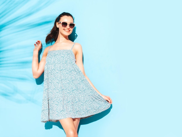 Joven hermosa mujer sonriente en vestido de verano de moda Mujer sexy despreocupada posando junto a la pared azul en el estudio Modelo morena positiva divirtiéndose Alegre y feliz Aislado