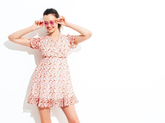 Joven hermosa mujer sonriente en vestido de verano de moda Mujer sexy despreocupada posando junto a la pared roja en el estudio Modelo morena positiva divirtiéndose y volviéndose loca Alegre y feliz