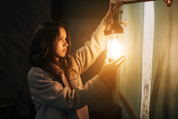 Joven hermosa mujer sostiene en su mano una pequeña lámpara de pared