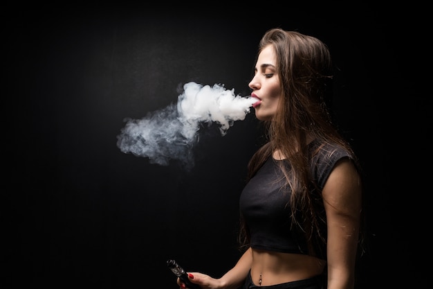Joven hermosa mujer vaping e - cigarrillo en la pared negra