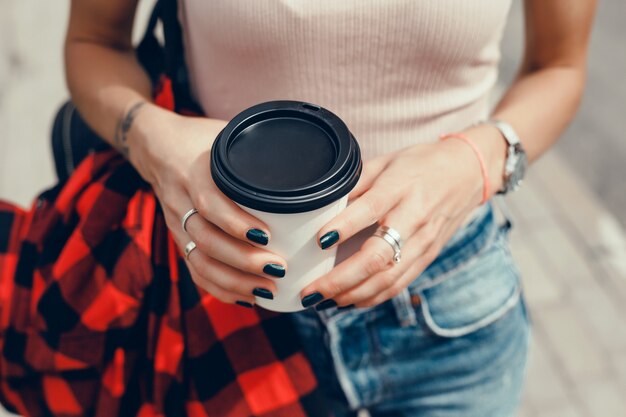 Joven hermosa niña bebe café en un vaso en la calle, se ríe y sonríe