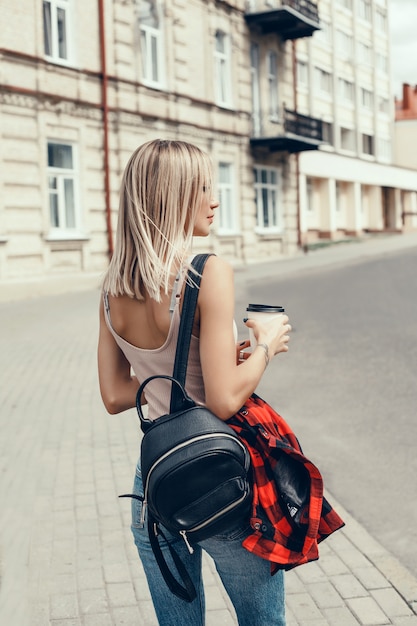 Joven hermosa niña bebe café en un vaso en la calle, se ríe y sonríe