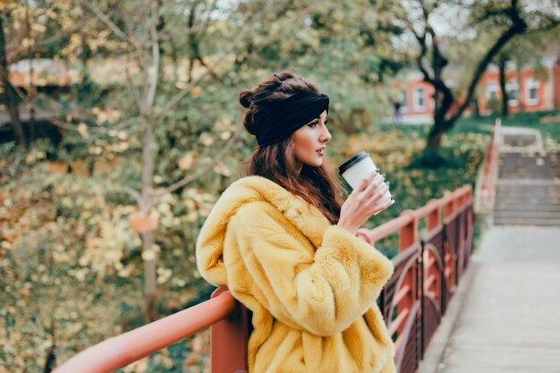 Joven hermosa niña bebe café en un vaso en la calle