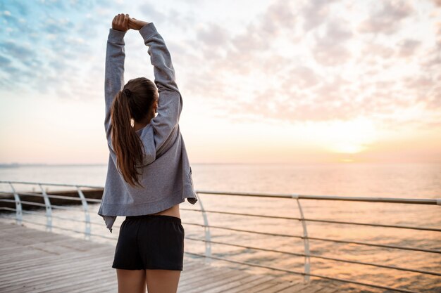 Joven hermosa niña deportiva entrenamiento al amanecer sobre el mar.