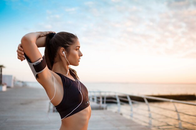 Joven hermosa niña deportiva entrenamiento al amanecer sobre el mar.