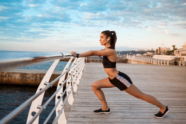 Joven hermosa niña deportiva entrenamiento al amanecer sobre el mar.