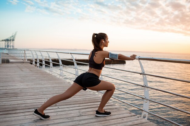 Joven hermosa niña deportiva entrenamiento al amanecer sobre el mar.