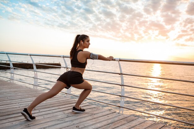 Joven hermosa niña deportiva entrenamiento al amanecer sobre el mar.