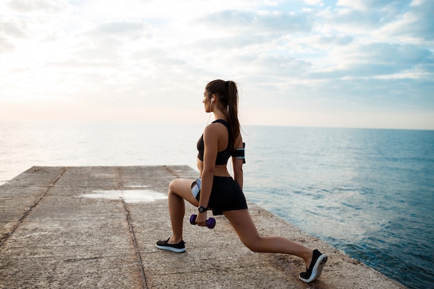 Joven hermosa niña deportiva entrenamiento al amanecer sobre el mar.