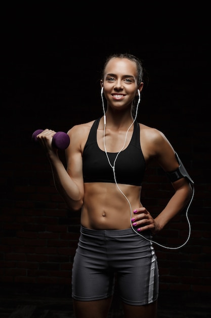 Foto gratuita joven hermosa niña deportiva sonriendo, entrenando sobre pared oscura