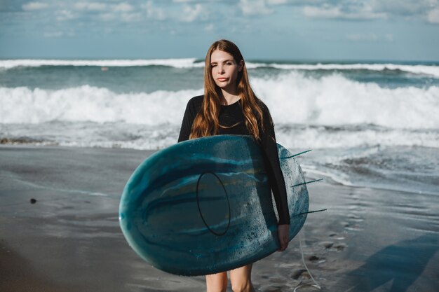 joven hermosa niña posando en la playa con una tabla de surf, surfista mujer, olas del océano