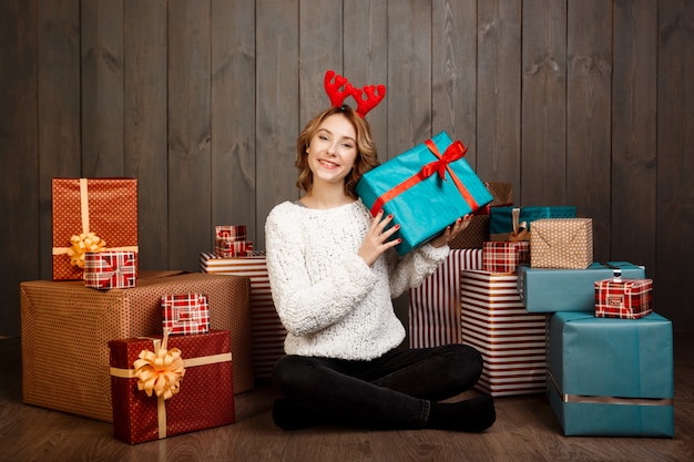 Joven hermosa niña sentada entre regalos de Navidad sobre pared de madera