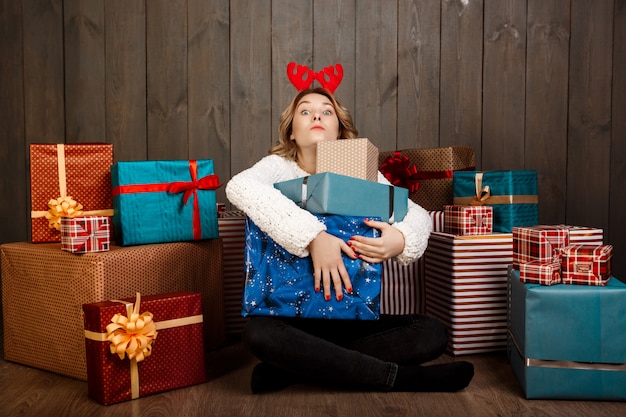 Joven hermosa niña sentada entre regalos de Navidad sobre pared de madera