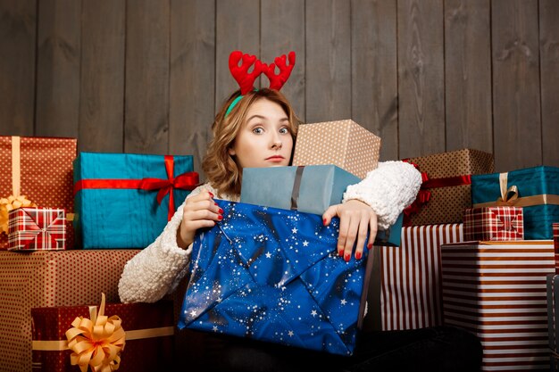 Joven hermosa niña sentada entre regalos de Navidad sobre pared de madera