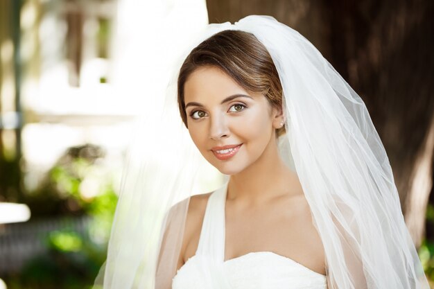 Joven hermosa novia rubia en vestido de novia y velo sonriendo.