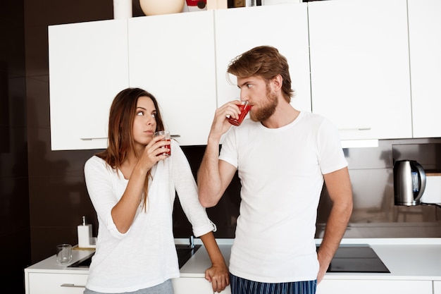 Joven hermosa pareja beber jugo de pie en la cocina.