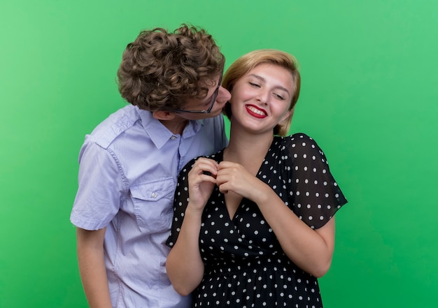Joven hermosa pareja feliz besando a su amada novia de pie sobre la pared verde