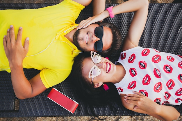 Joven hermosa pareja hipster enamorada, acostado abrazando, escuchando música, gafas de sol, traje elegante, vacaciones de verano, divirtiéndose, sonriendo, feliz, colorido, vista desde arriba